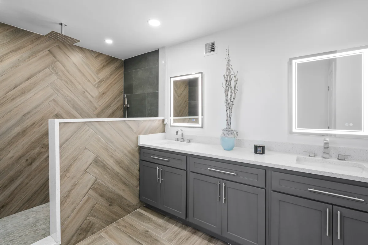 Gray bathroom vanity beside a herringbone tile shower